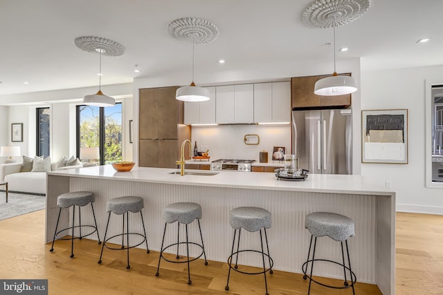 kitchen with light countertops, white cabinetry, freestanding refrigerator, a kitchen bar, and a sink