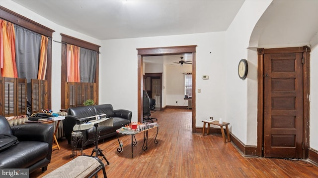living room featuring hardwood / wood-style floors, ceiling fan, baseboards, and arched walkways