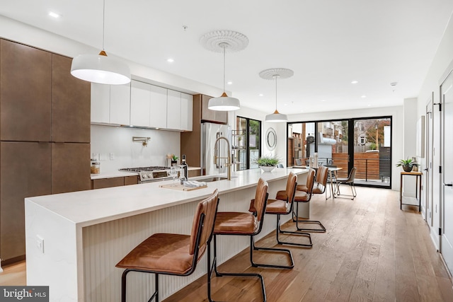 kitchen with light wood-type flooring, light countertops, a wealth of natural light, a center island with sink, and modern cabinets