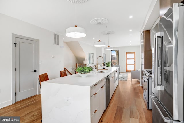 kitchen with modern cabinets, a sink, light wood-type flooring, appliances with stainless steel finishes, and a kitchen island with sink