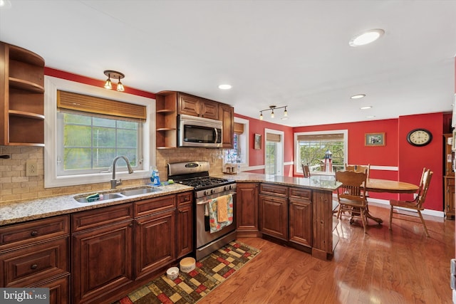 kitchen with open shelves, a sink, stainless steel appliances, a peninsula, and light wood-type flooring