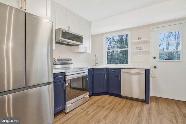 kitchen with a sink, appliances with stainless steel finishes, blue cabinetry, and light wood finished floors