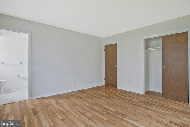 unfurnished bedroom featuring a closet, light wood finished floors, baseboards, and ensuite bathroom