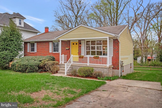 view of front of house with a front yard, brick siding, a chimney, and covered porch