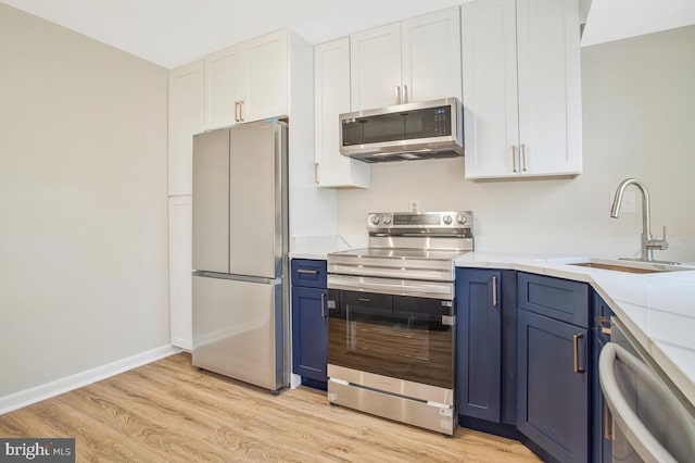 kitchen featuring light wood-style flooring, appliances with stainless steel finishes, a sink, and blue cabinetry