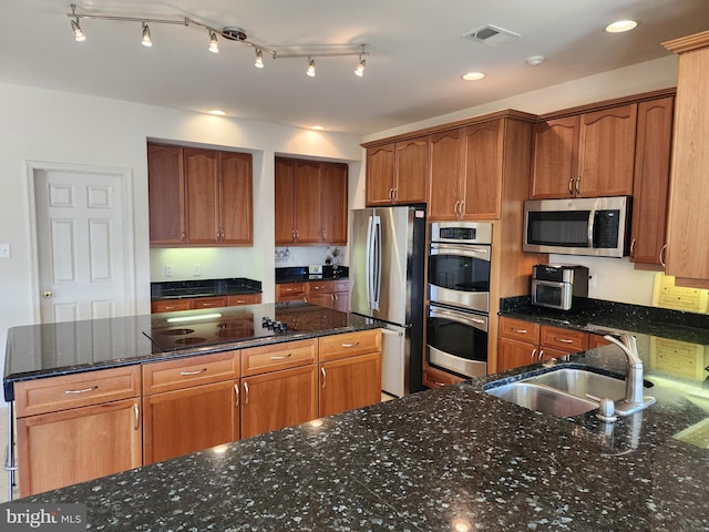 kitchen with dark stone countertops, a sink, brown cabinetry, appliances with stainless steel finishes, and visible vents