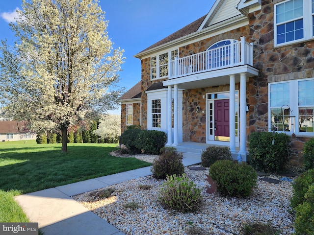 property entrance with stone siding, a balcony, a yard, and roof with shingles