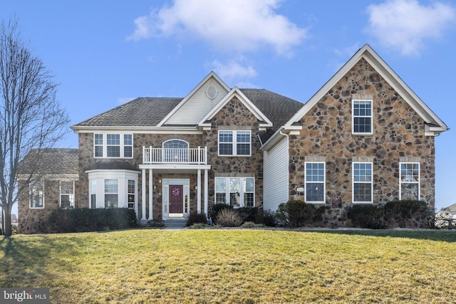 view of front of house with roof with shingles, stone siding, a front yard, and a balcony
