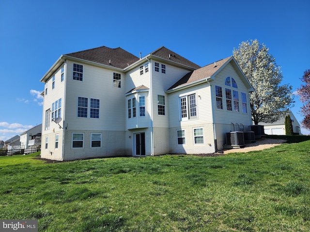 back of house featuring fence, a lawn, brick siding, and central AC unit