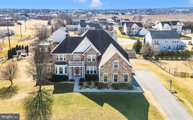 view of front of property with fence, a balcony, a residential view, stone siding, and a front yard