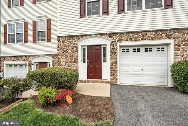 property entrance featuring a garage, aphalt driveway, and stone siding