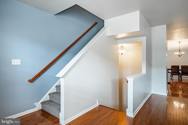 staircase featuring baseboards, a chandelier, and hardwood / wood-style flooring