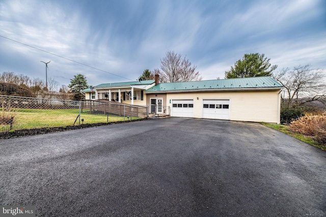ranch-style house with aphalt driveway, metal roof, fence, an attached garage, and a chimney
