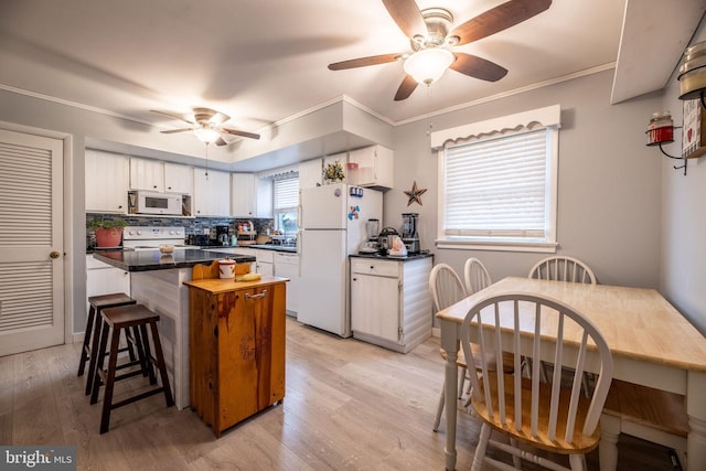 kitchen featuring ceiling fan, white appliances, a kitchen bar, dark countertops, and backsplash