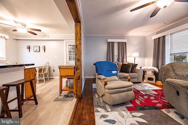 living room with light wood-style flooring, ornamental molding, baseboards, and a ceiling fan