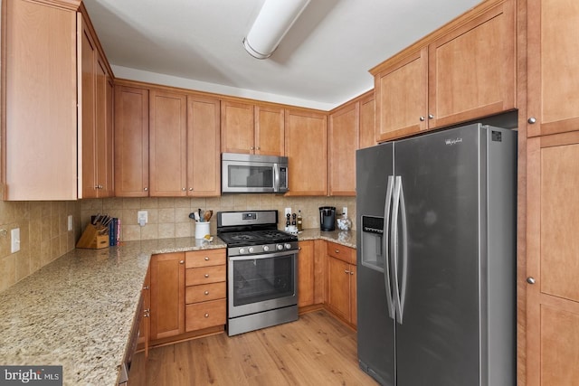 kitchen with appliances with stainless steel finishes, backsplash, light stone countertops, and light wood-style floors