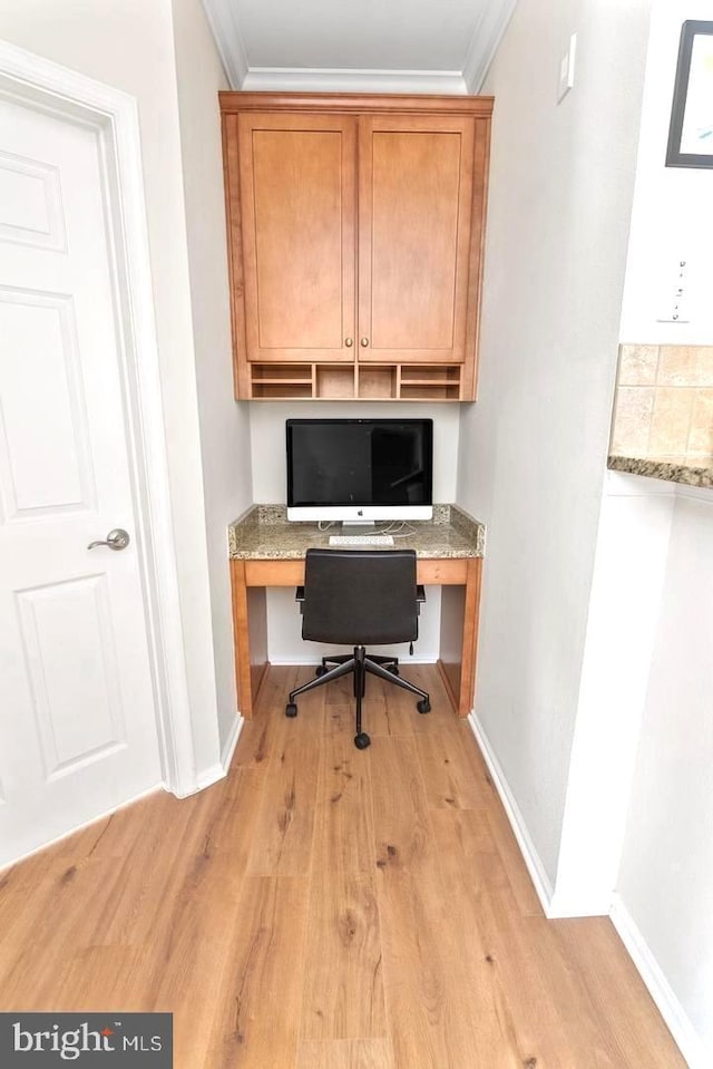 office area with built in desk, light wood-style floors, ornamental molding, and baseboards