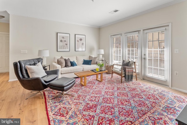 living room featuring light wood-type flooring, crown molding, and baseboards
