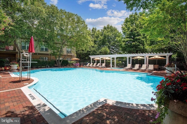 community pool featuring a pergola, fence, a patio, and view of wooded area