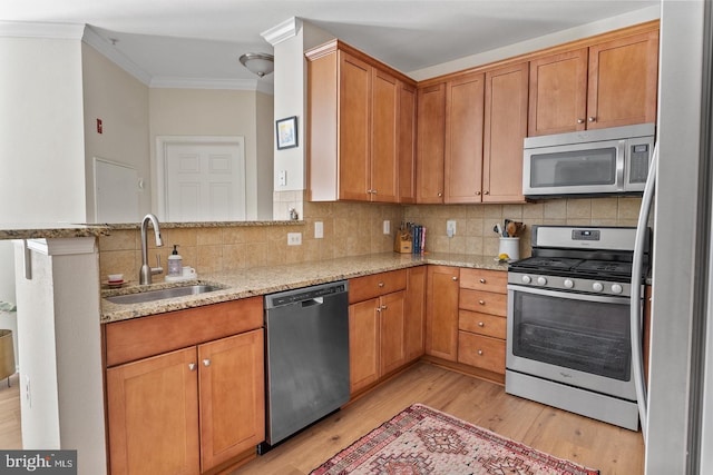 kitchen with stainless steel appliances, a sink, crown molding, light wood-style flooring, and light stone countertops