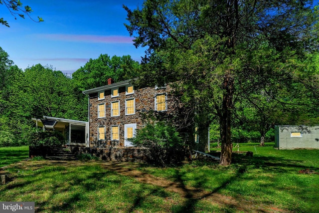 view of front facade featuring stone siding, a chimney, and a lawn