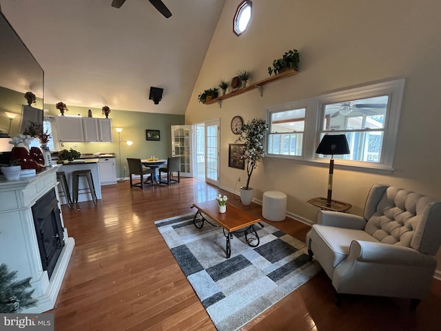 living room with a ceiling fan, high vaulted ceiling, baseboards, and dark wood finished floors
