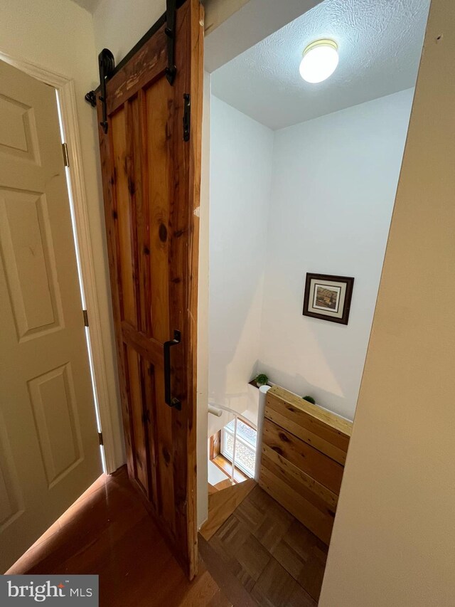 hallway with parquet flooring, a barn door, an upstairs landing, and a textured ceiling