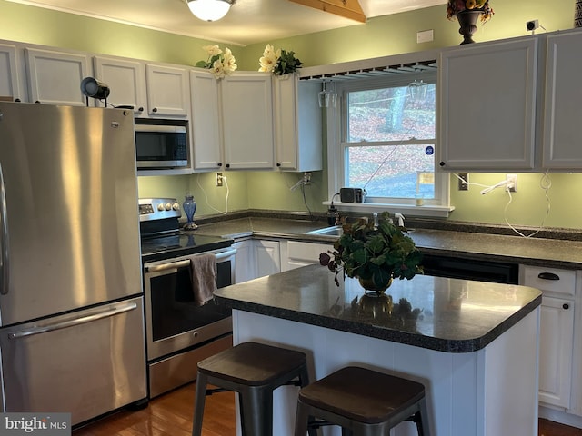 kitchen with white cabinets, dark countertops, dark wood finished floors, appliances with stainless steel finishes, and a center island