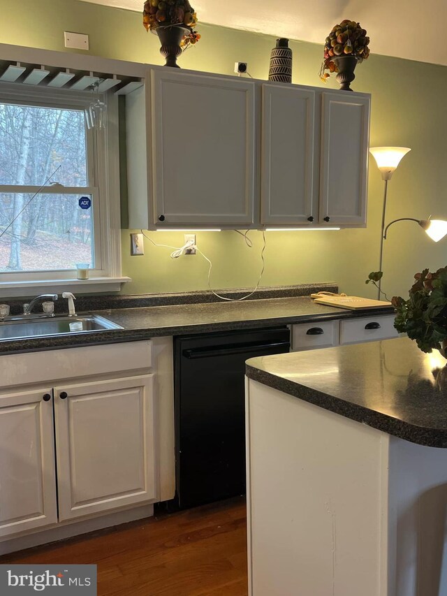 kitchen with a sink, white cabinetry, dark wood finished floors, black dishwasher, and dark countertops