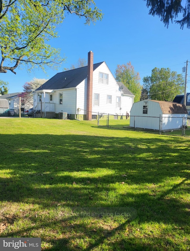 back of property with a chimney, fence, central AC, and a lawn