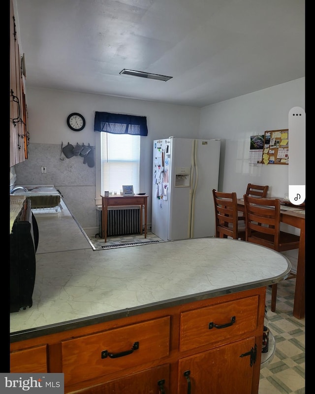 kitchen featuring white fridge with ice dispenser, brown cabinetry, and a peninsula