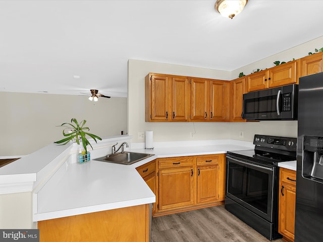 kitchen with light countertops, a sink, light wood-type flooring, black appliances, and a peninsula