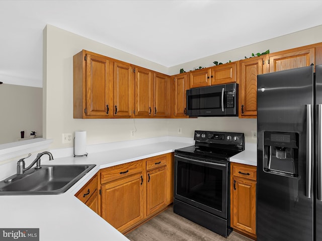 kitchen featuring brown cabinets, light countertops, a sink, stainless steel fridge, and black electric range oven