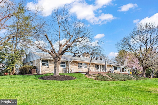 back of property with stone siding, a deck, and a lawn
