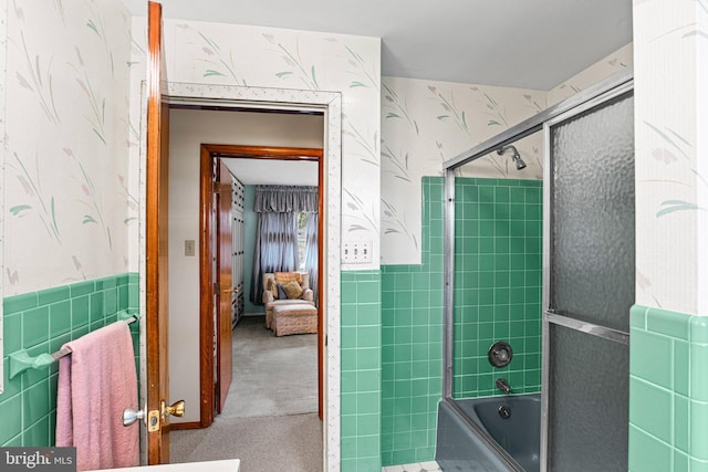 full bathroom with tile walls, a wainscoted wall, wallpapered walls, and bath / shower combo with glass door