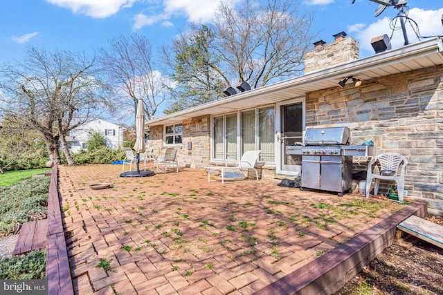 rear view of property with a patio area, a chimney, and stone siding
