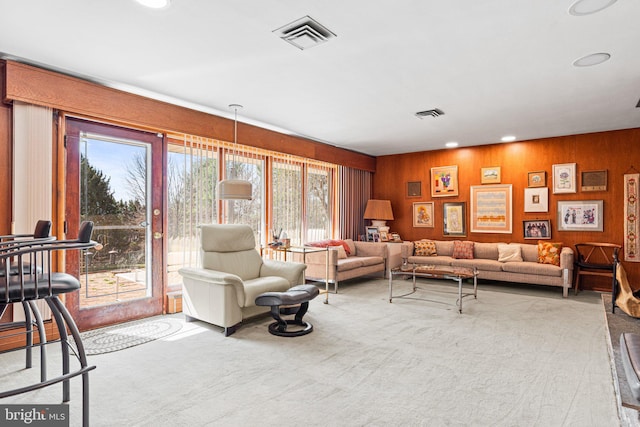 carpeted living room with visible vents, wood walls, and recessed lighting