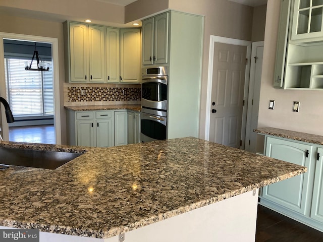 kitchen with dark wood-style flooring, backsplash, dark stone counters, double oven, and a sink