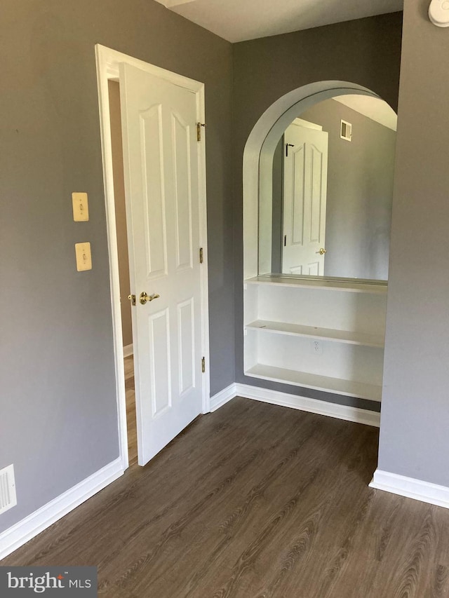 spare room with arched walkways, dark wood-type flooring, and baseboards
