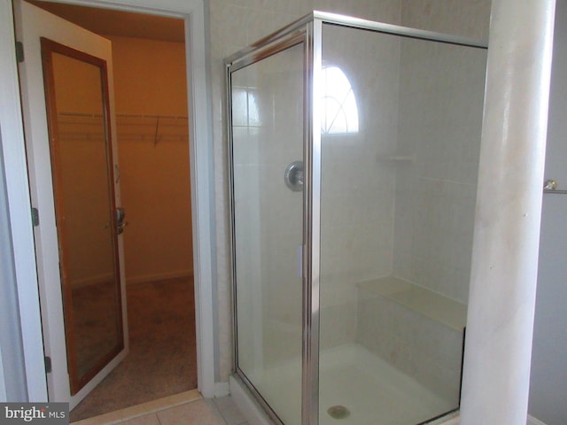 bathroom with a stall shower, a walk in closet, and tile patterned floors