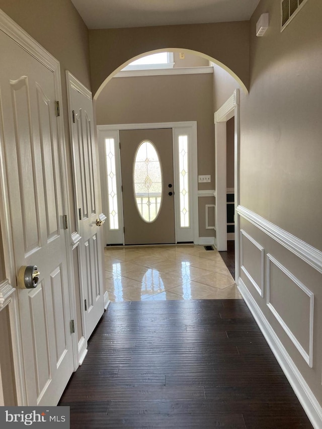 foyer featuring arched walkways, a decorative wall, visible vents, and a wainscoted wall