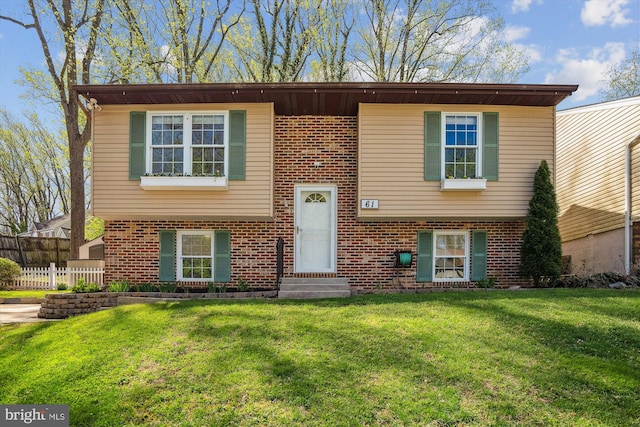 bi-level home featuring a front yard, fence, and brick siding