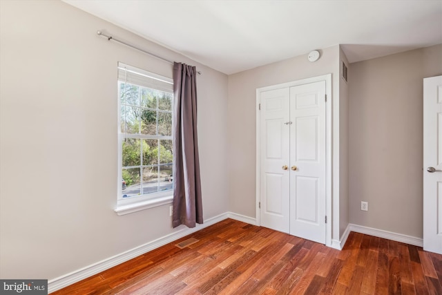 unfurnished bedroom featuring a closet, baseboards, multiple windows, and wood finished floors