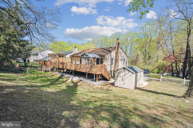 back of house featuring a chimney, a shed, a fenced backyard, a wooden deck, and an outbuilding