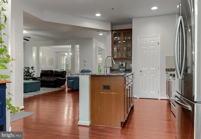 kitchen with glass insert cabinets, open floor plan, freestanding refrigerator, wood finished floors, and backsplash
