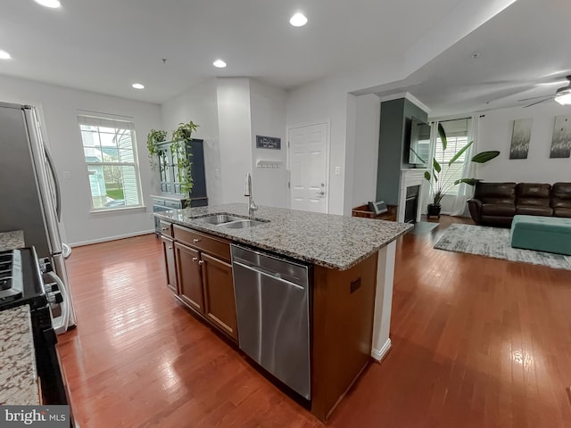 kitchen with a sink, an island with sink, wood finished floors, light stone countertops, and stainless steel appliances