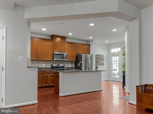 kitchen with stainless steel appliances, dark wood-style flooring, brown cabinets, and backsplash