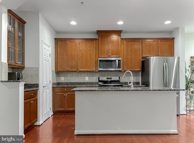 kitchen with stainless steel appliances, dark wood-style floors, and dark stone countertops