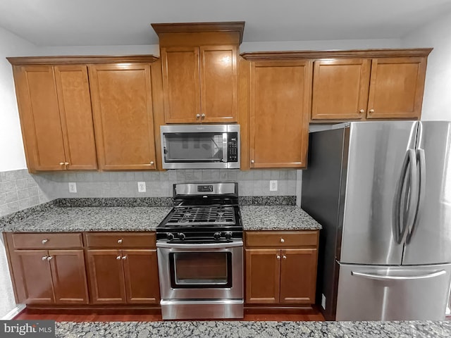 kitchen with dark wood-style flooring, light stone countertops, brown cabinetry, decorative backsplash, and appliances with stainless steel finishes