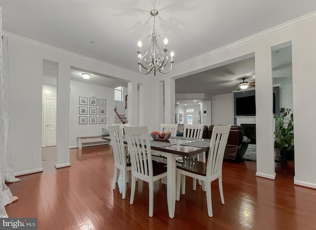 dining space with crown molding, ceiling fan with notable chandelier, a fireplace, stairway, and wood-type flooring